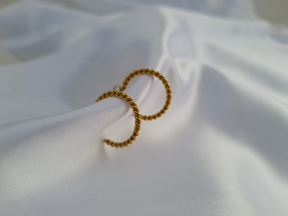 A pair of gold twisted rope hoop earrings resting on draped white satin fabric.