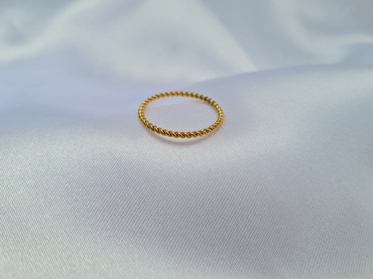 A thin gold rope-style ring resting on a white satin fabric background.